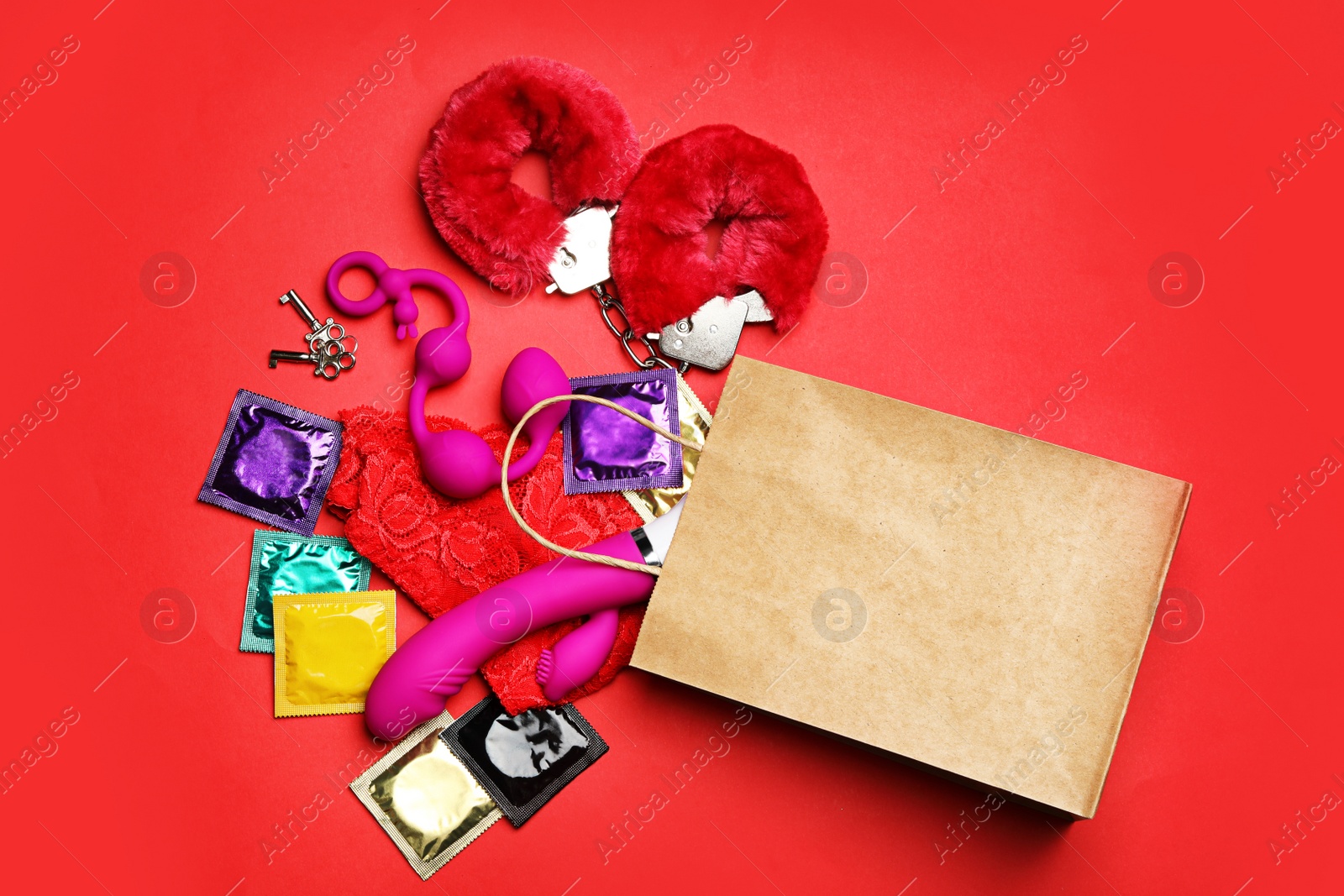 Photo of Shopping bag and different sex toys on red background, flat lay