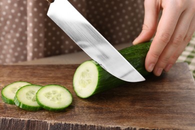 Photo of Woman cutting cucumber on wooden board, closeup