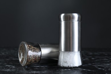 Pepper and salt shakers on dark marble table, closeup