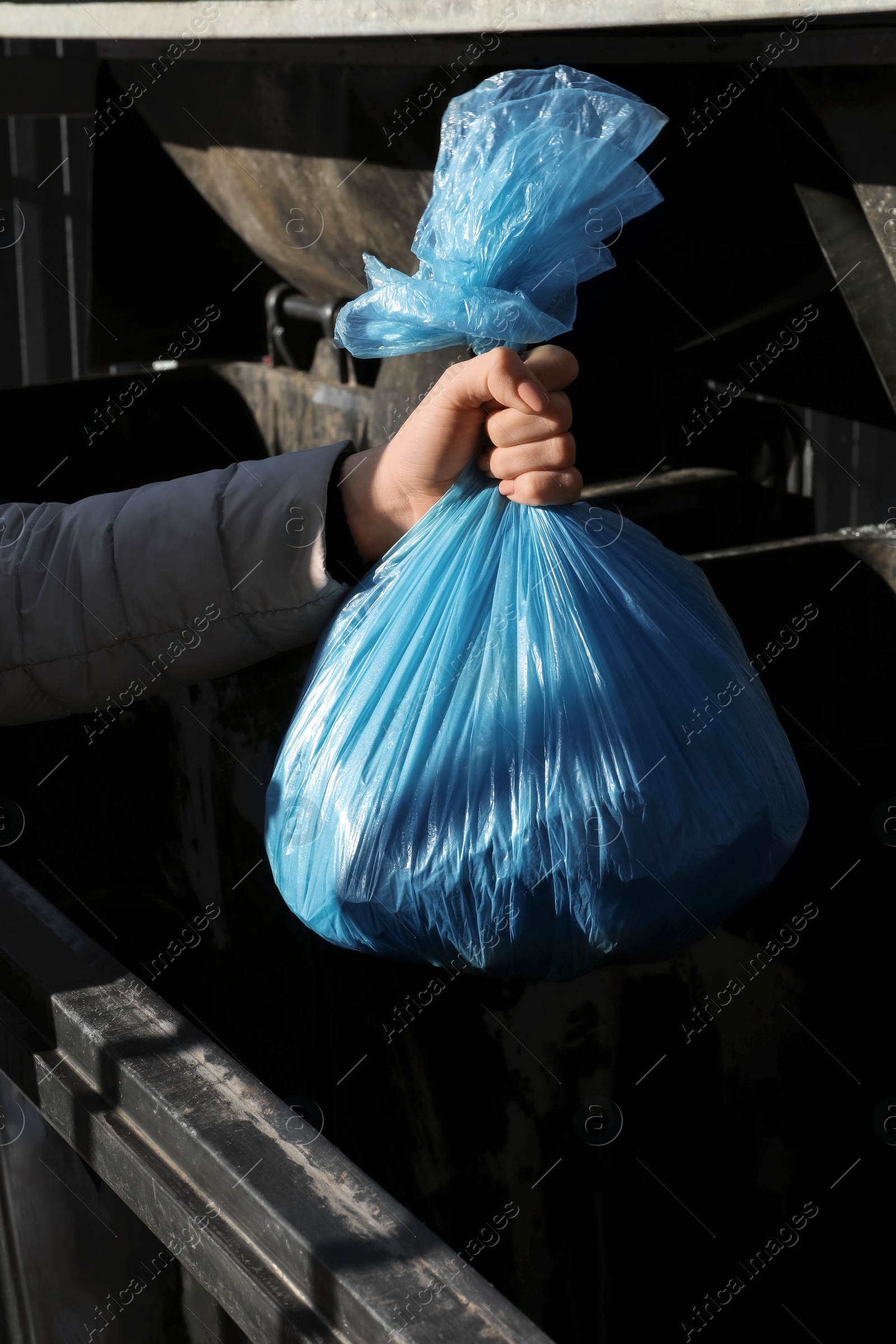 Photo of Woman throwing trash bag full of garbage in bin outdoors, closeup