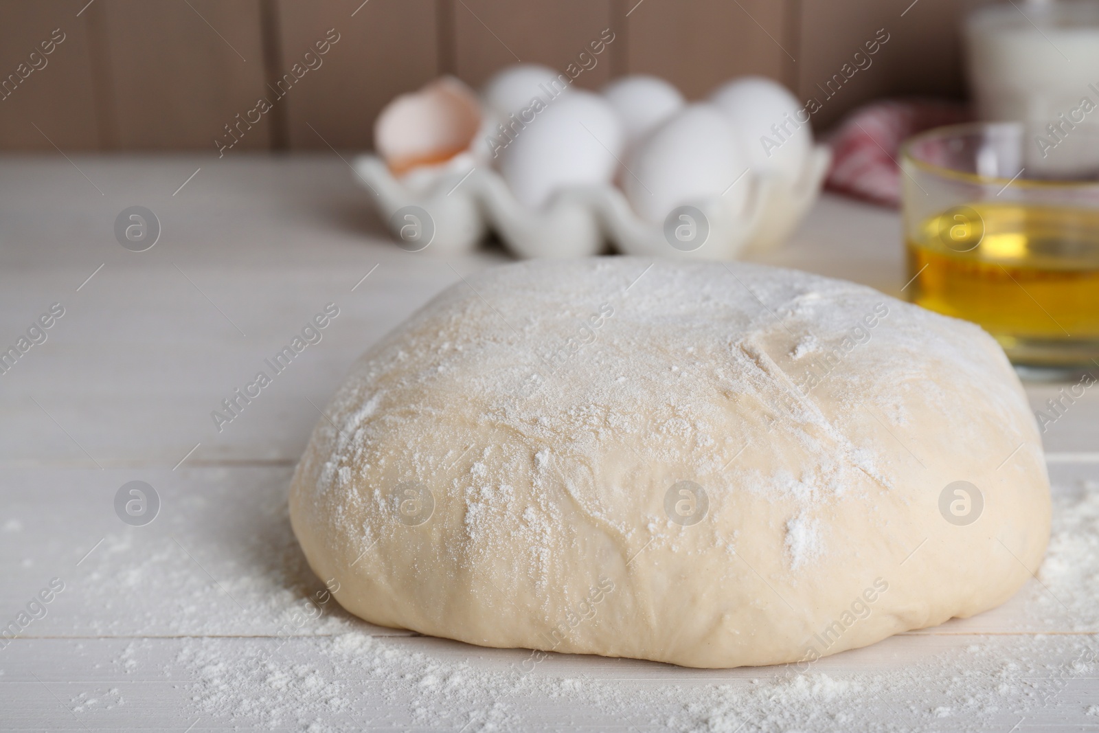 Photo of Fresh yeast dough with flour on white wooden table, closeup. Space for text