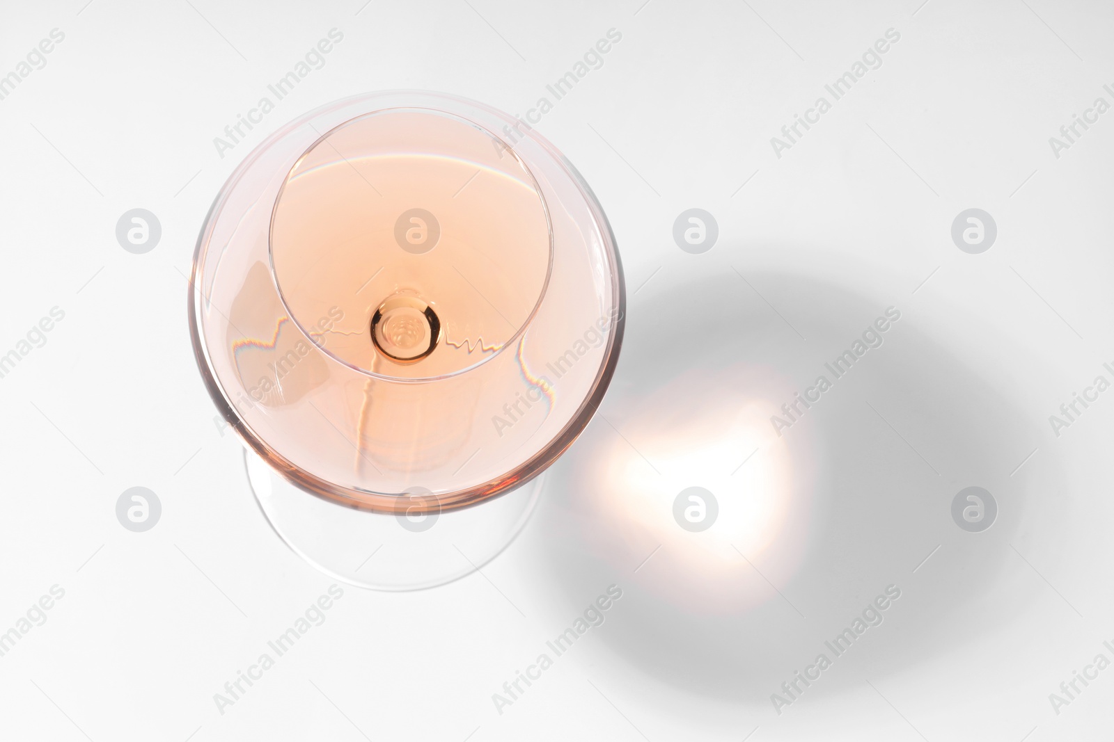 Photo of Rose wine in glass and shadow on white background, top view. Space for text