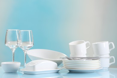 Set of many clean dishware, cutlery and glasses on light blue table