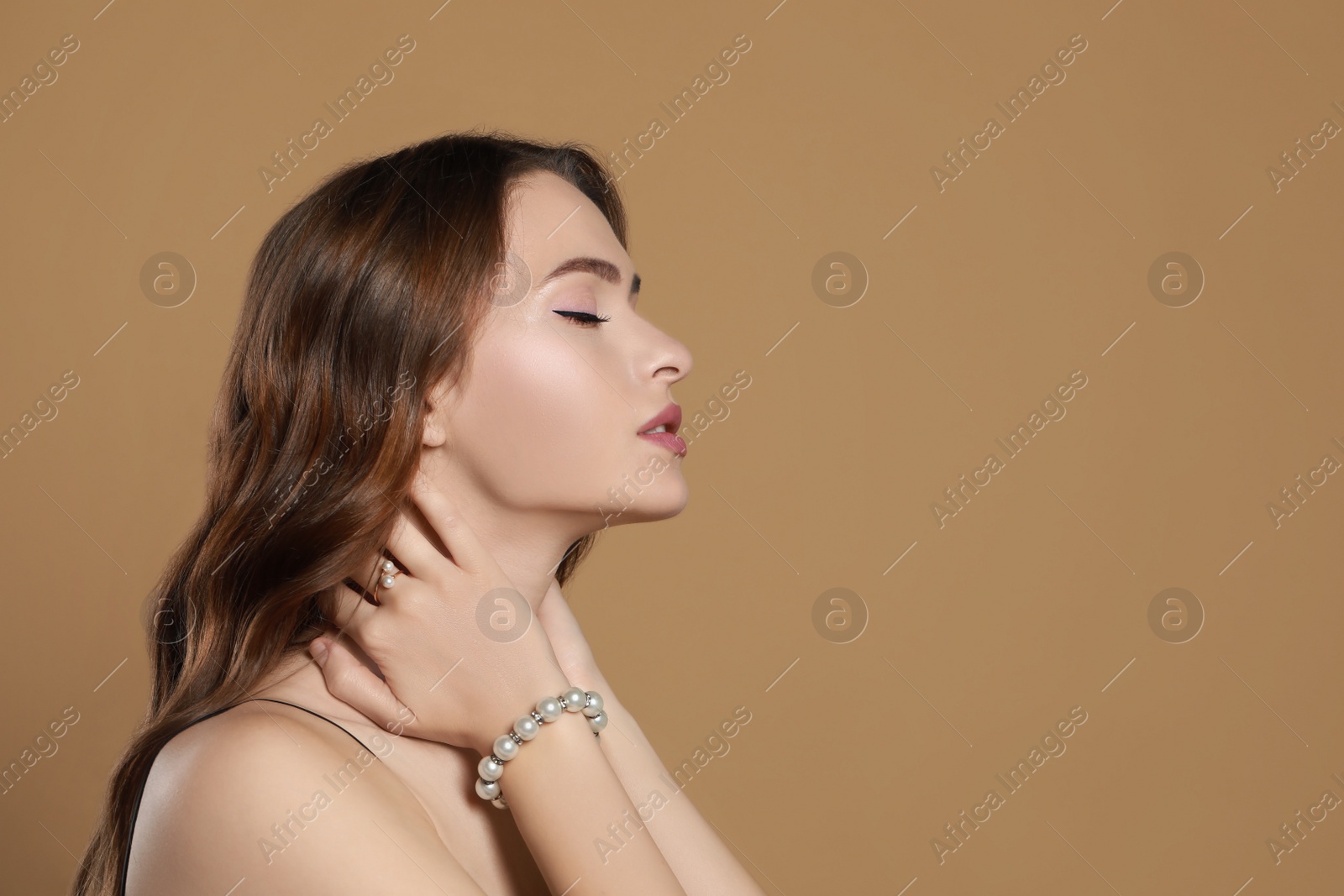 Photo of Young woman wearing elegant pearl jewelry on brown background, space for text