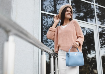 Young woman with stylish light blue bag near railing outdoors