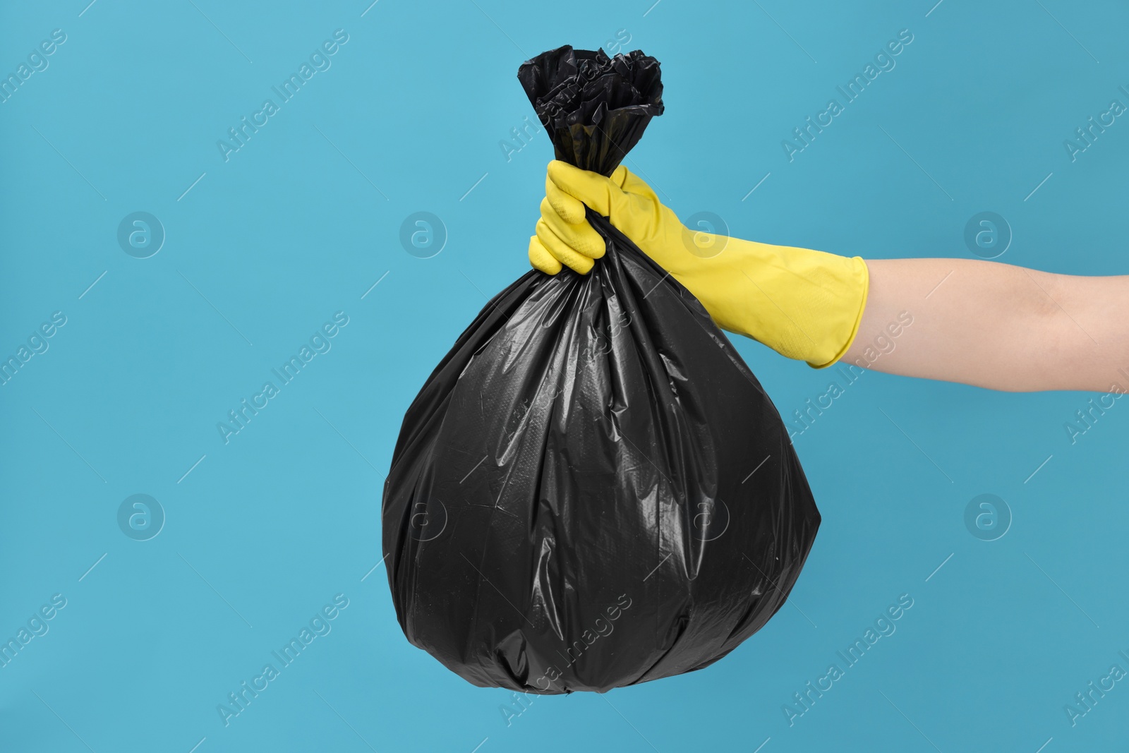 Photo of Woman holding plastic bag full of garbage on light blue background, closeup