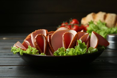 Photo of Slices of delicious boiled sausage with lettuce on dark wooden table, closeup
