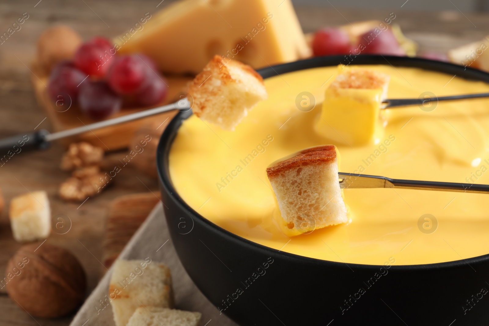 Photo of Dipping pieces of bread into tasty cheese fondue at table, closeup