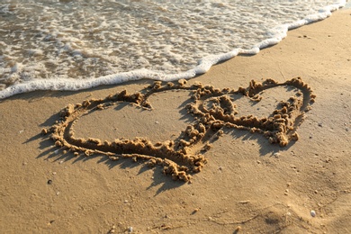 Hearts drawn on sandy beach near sea. Wedding concept