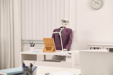 Human skeleton in suit at table in office