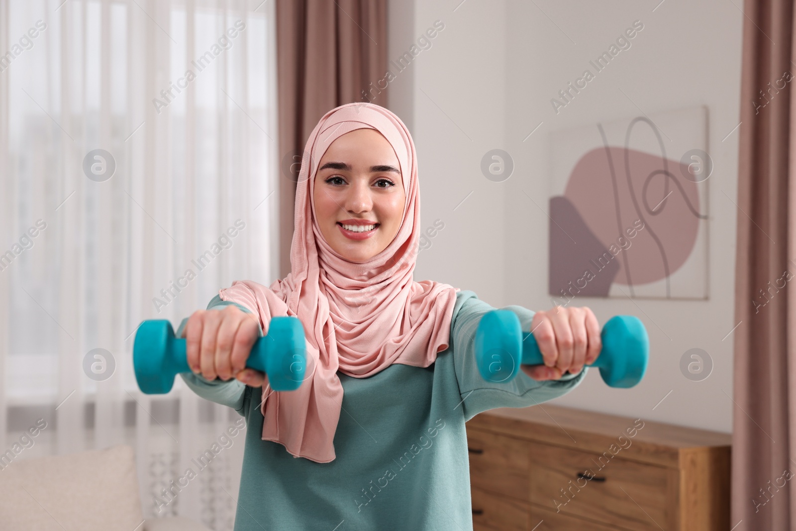 Photo of Muslim woman in hijab doing exercise with dumbbells at home