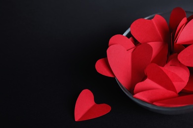 Photo of Red paper hearts in bowl on black background. Space for text