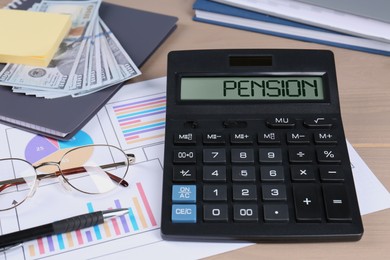 Photo of Calculator, dollar banknotes, papers, glasses, pen and notebook on wooden table. Pension planning