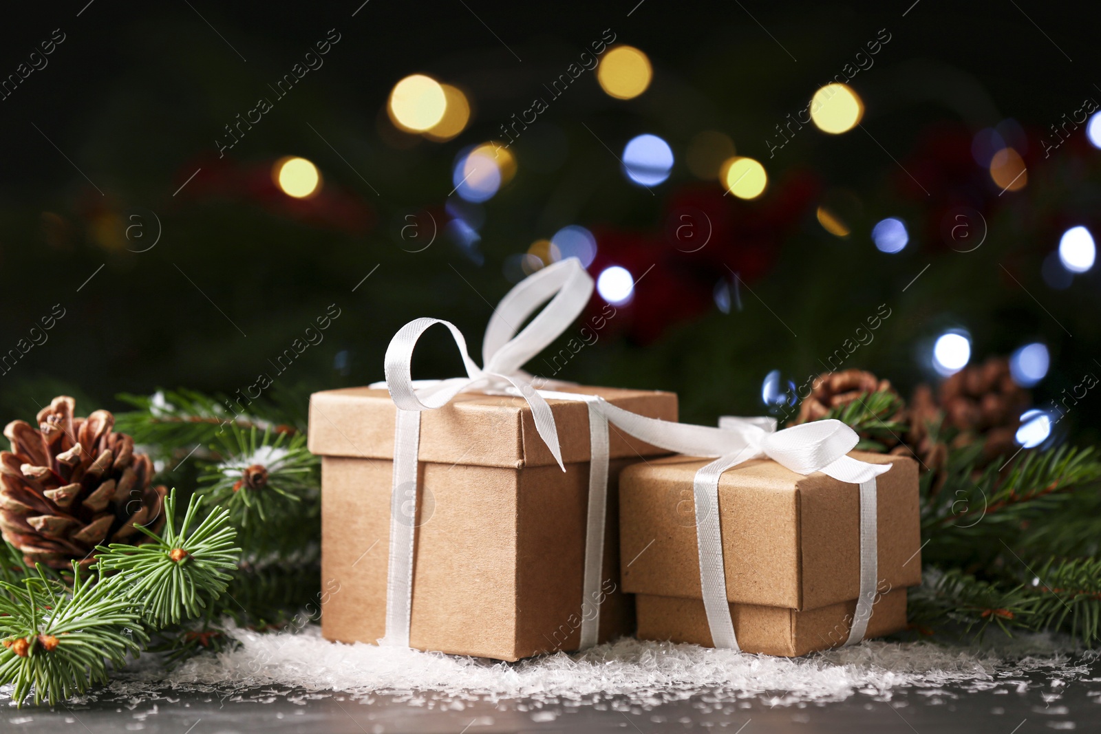 Photo of Christmas present. Beautiful gift boxes, artificial snow and fir tree branches on black table against blurred festive lights