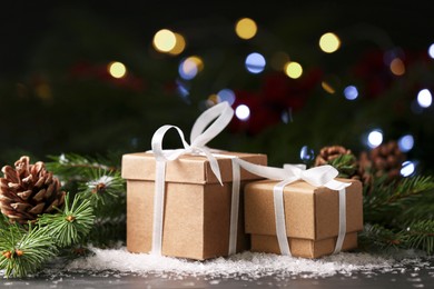 Photo of Christmas present. Beautiful gift boxes, artificial snow and fir tree branches on black table against blurred festive lights