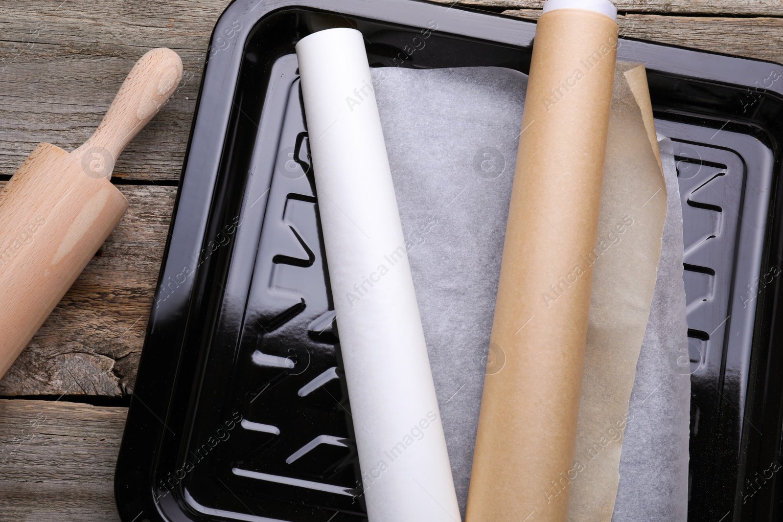 Photo of Rolls of parchment paper in baking pan and rolling pin on wooden table, flat lay