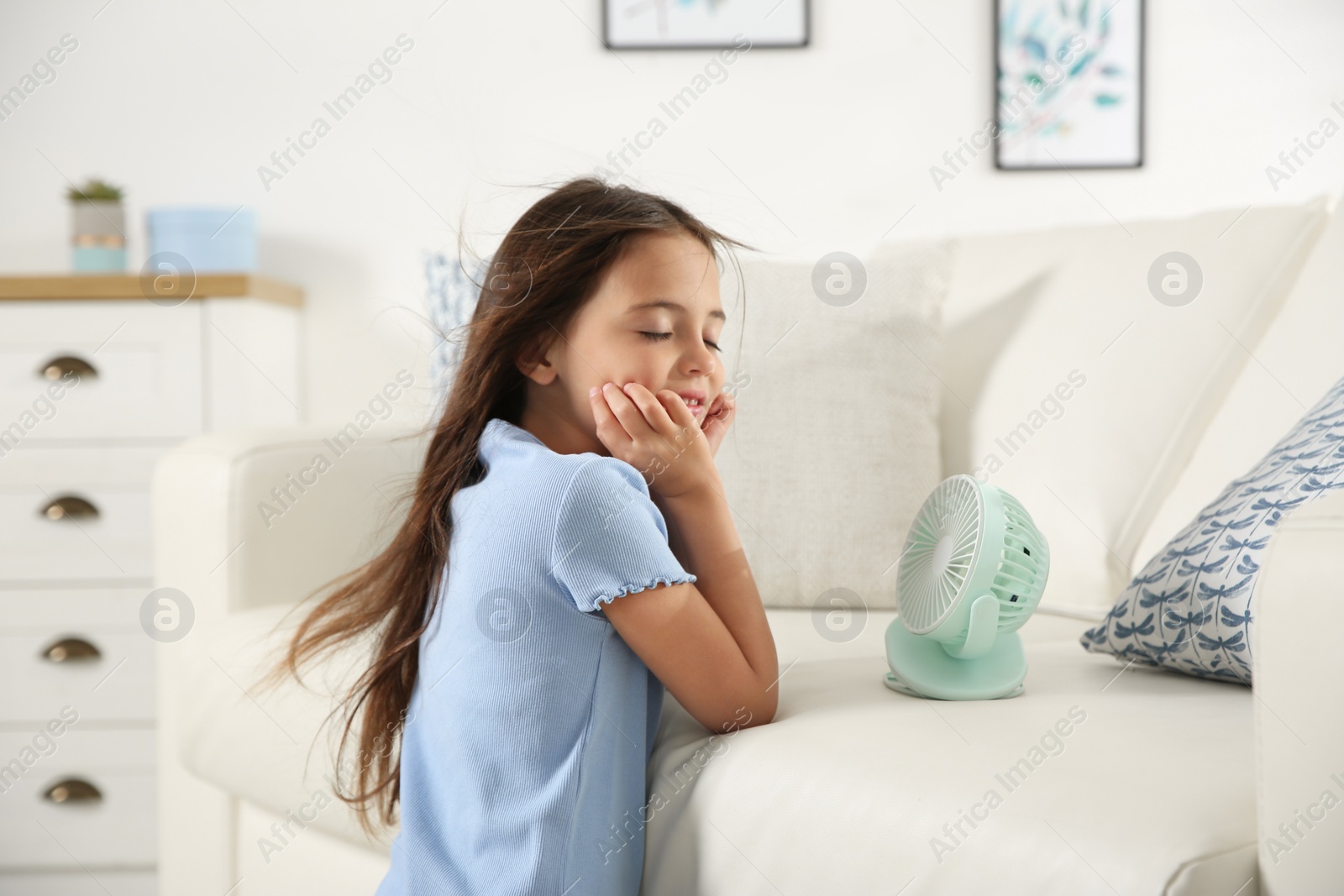 Photo of Little girl enjoying air flow from portable fan at home. Summer heat