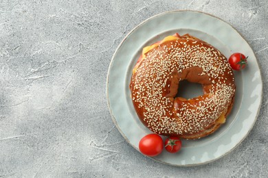 Photo of Delicious bagel with ham, cheese and tomatoes on light grey textured table, top view. Space for text
