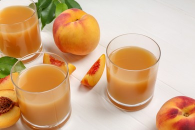 Glasses of peach juice, fresh fruits and leaves on white wooden table