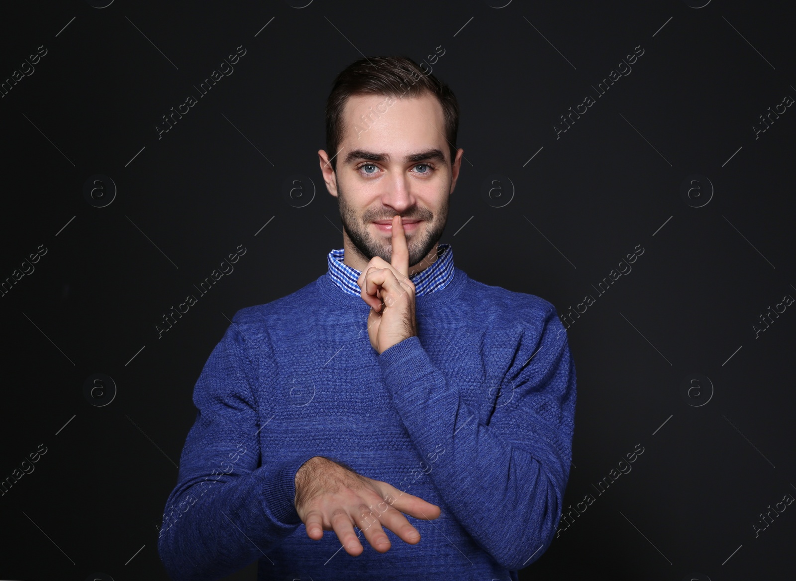 Photo of Man showing HUSH gesture in sign language on black background