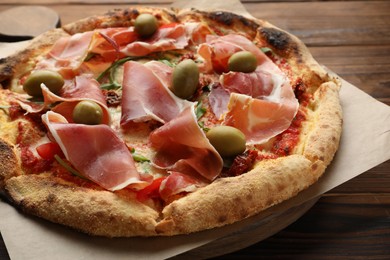 Photo of Tasty pizza with cured ham, olives and sun-dried tomato on wooden table, closeup