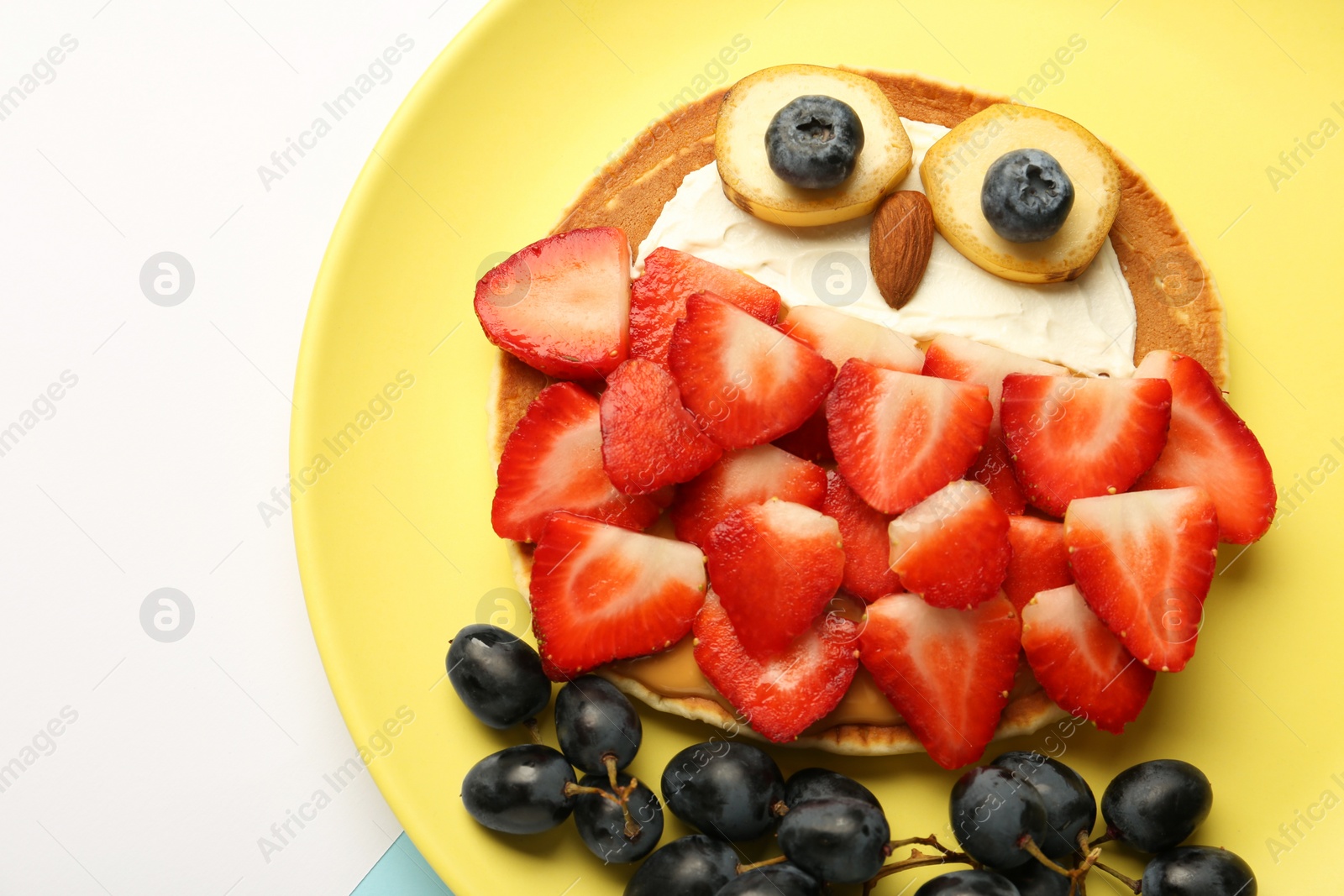 Photo of Creative serving for kids. Plate with cute owl made of pancakes, berries, cream, banana and almond on white table, top view