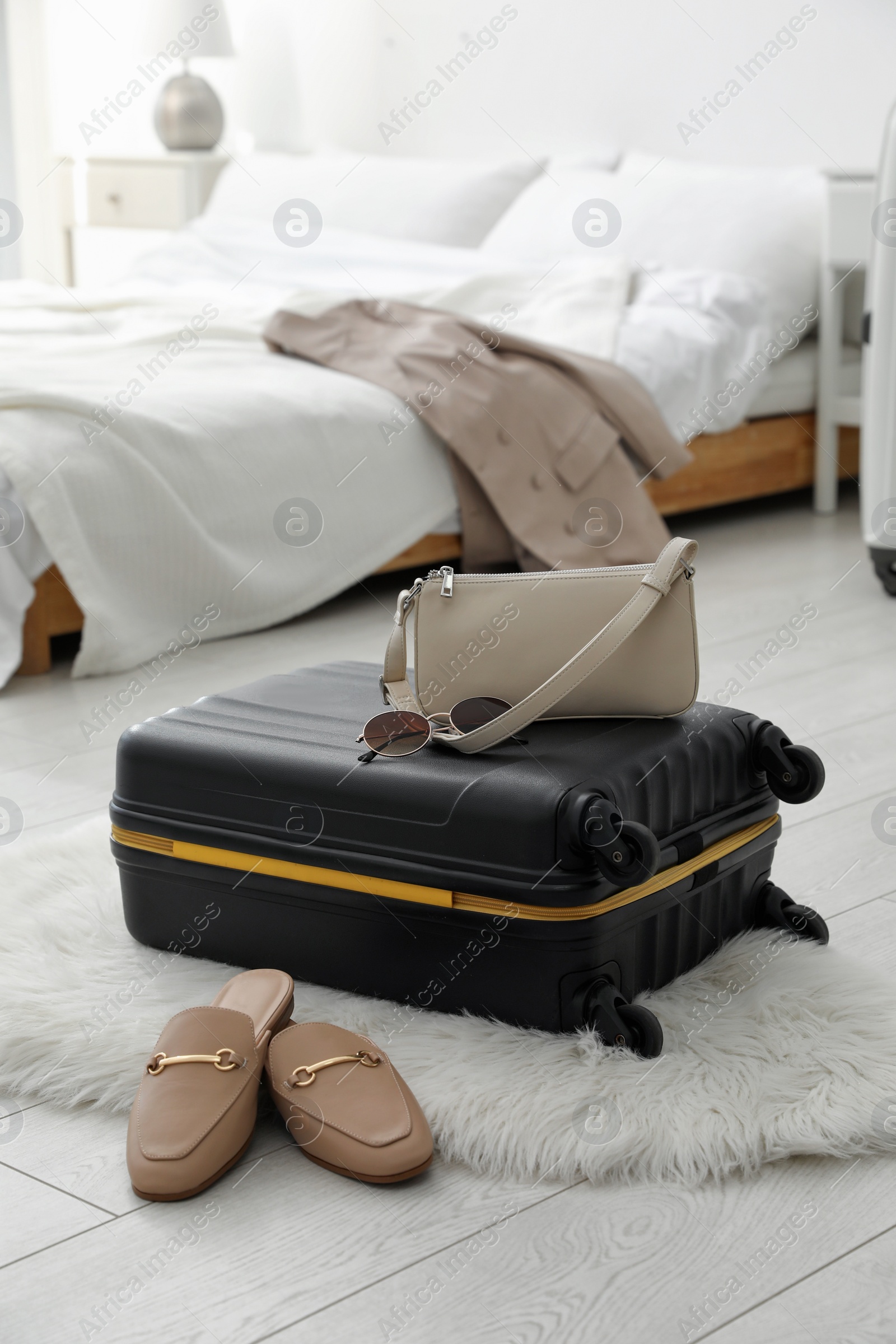 Photo of Suitcase packed for trip, shoes and fashionable accessories on floor in bedroom