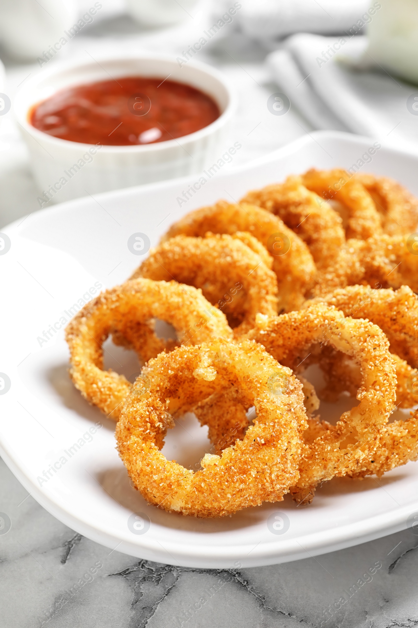 Photo of Plate with homemade crunchy fried onion rings and sauce on marble table, closeup