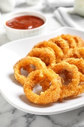 Photo of Plate with homemade crunchy fried onion rings and sauce on marble table, closeup