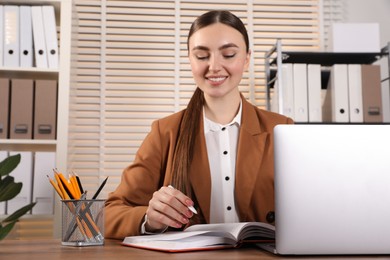 Photo of Happy woman taking notes at wooden table in office