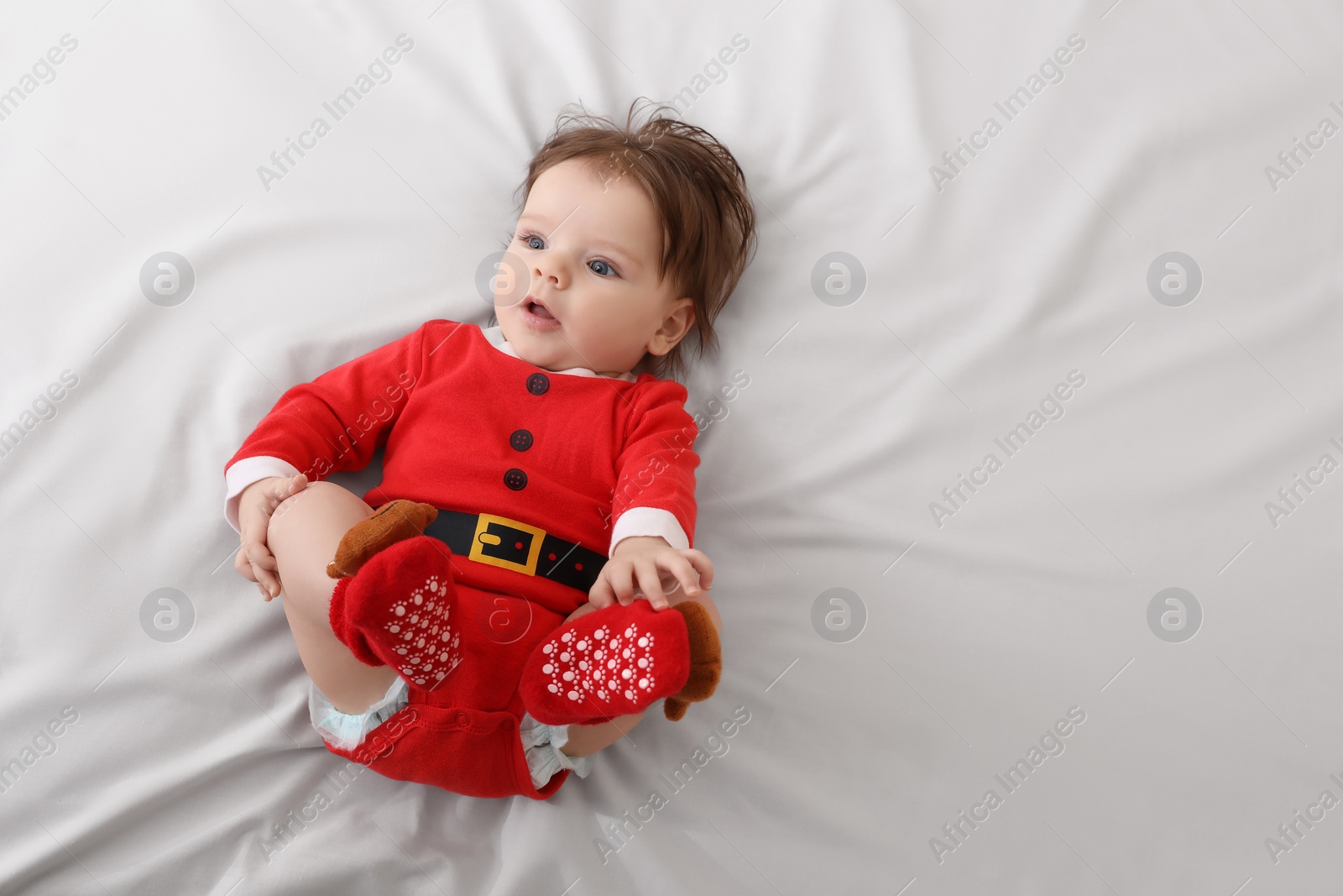 Photo of Cute baby wearing festive Christmas costume on white bedsheet, top view. Space for text