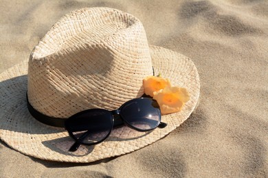 Photo of Hat with beautiful sunglasses and flowers on sand, closeup