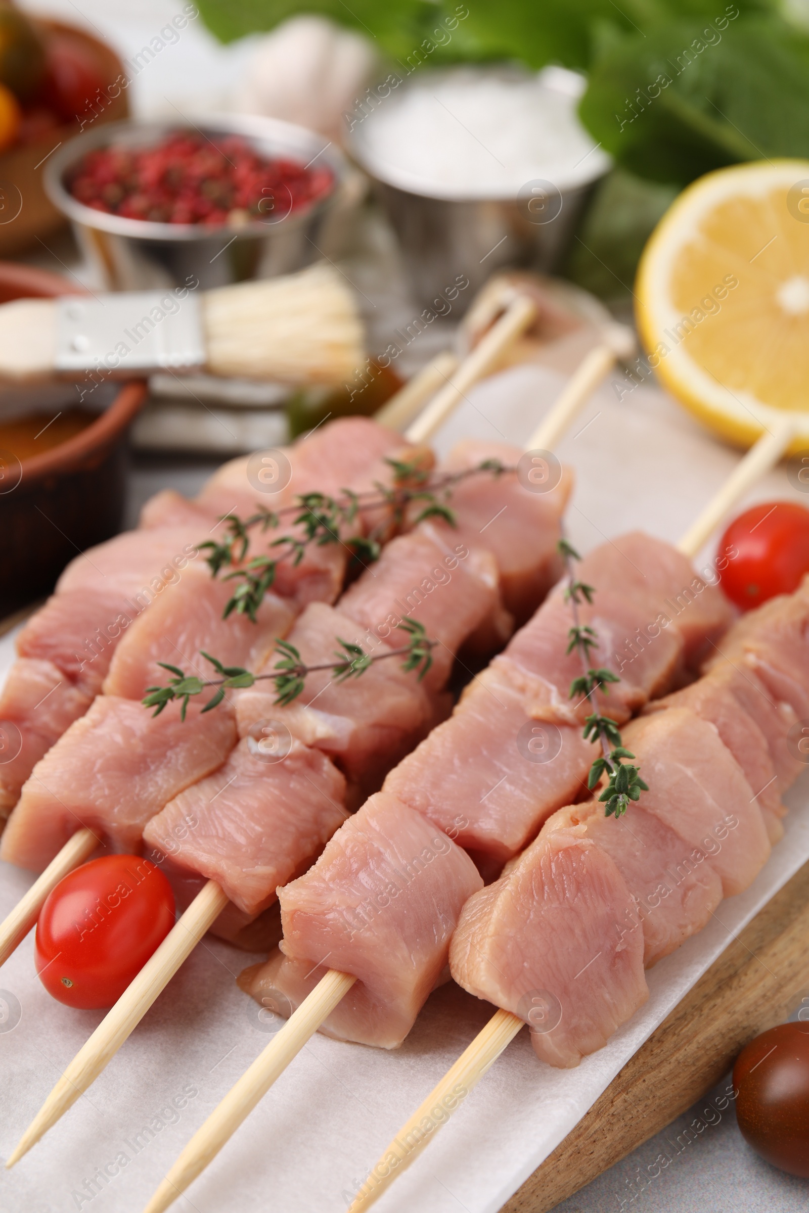 Photo of Skewers with cut raw meat, thyme and tomatoes on table, closeup