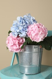 Photo of Beautiful hortensia flowers in bucket on chair near beige wall