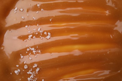 Delicious caramel sauce with sea salt as background, closeup