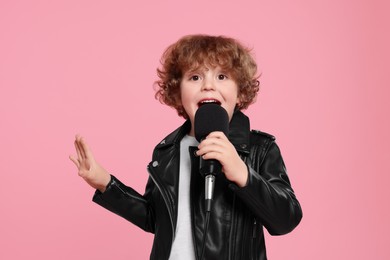 Photo of Cute little boy with microphone singing on pink background