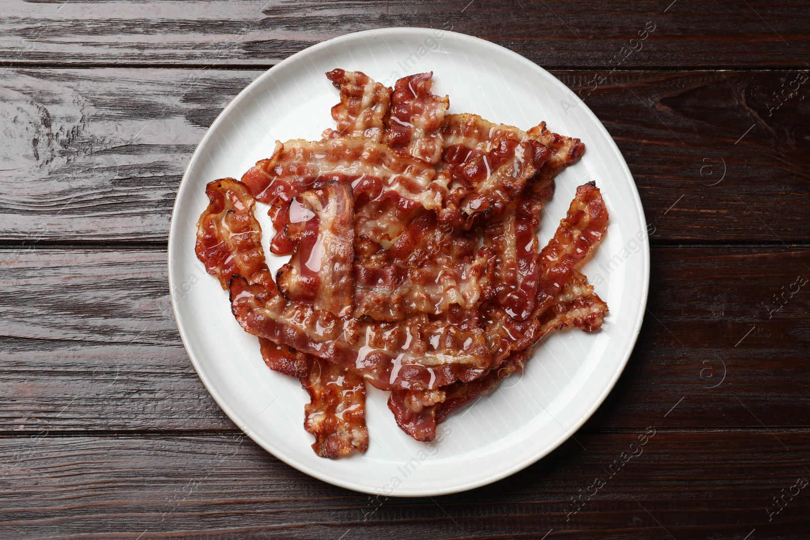 Photo of Slices of tasty fried bacon on wooden table, top view