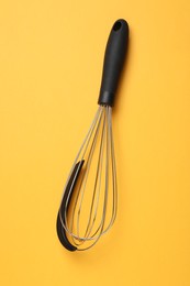 Photo of Metal whisk on yellow background, top view. Kitchen tool