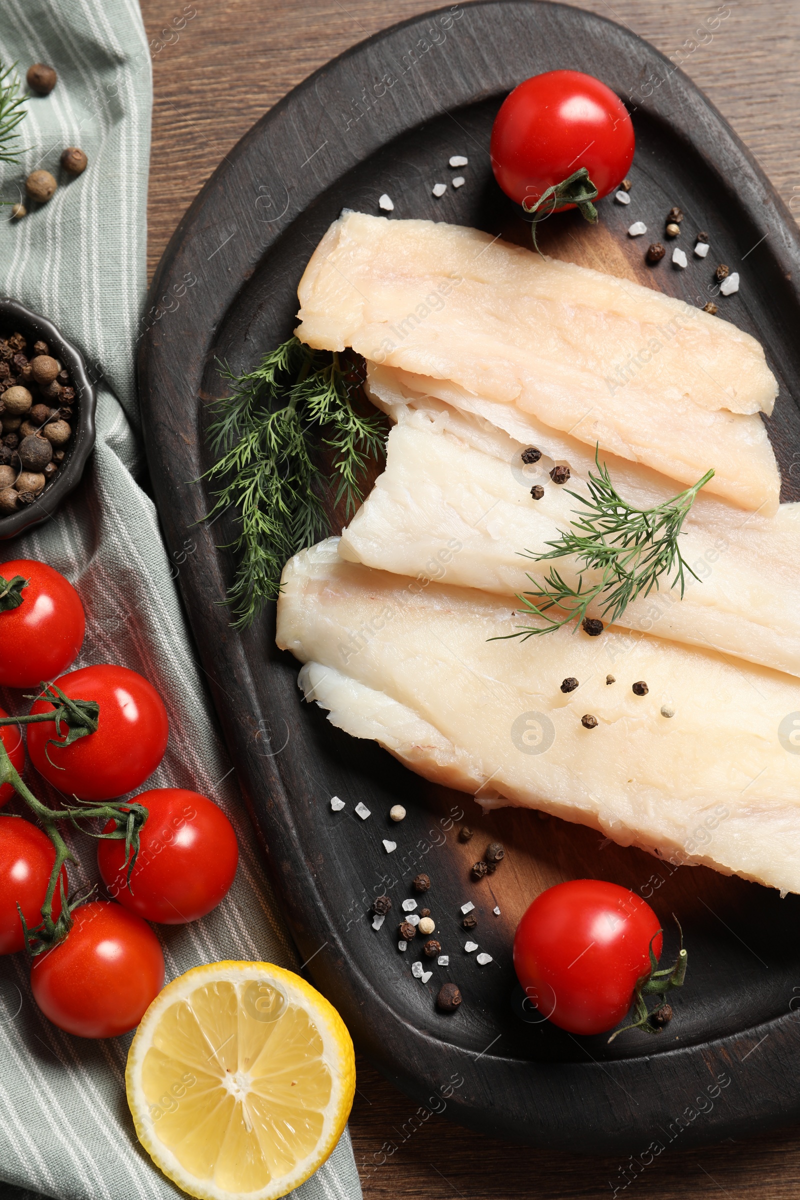 Photo of Raw cod fish, dill, lemon, tomatoes and spices on wooden table, top view