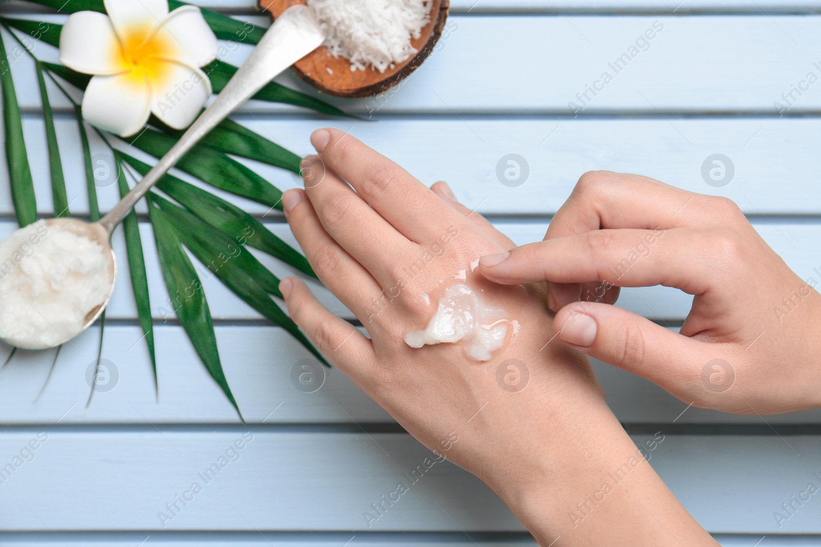 Photo of Young woman applying coconut oil on wooden background, closeup