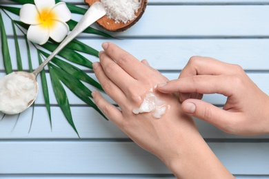 Photo of Young woman applying coconut oil on wooden background, closeup