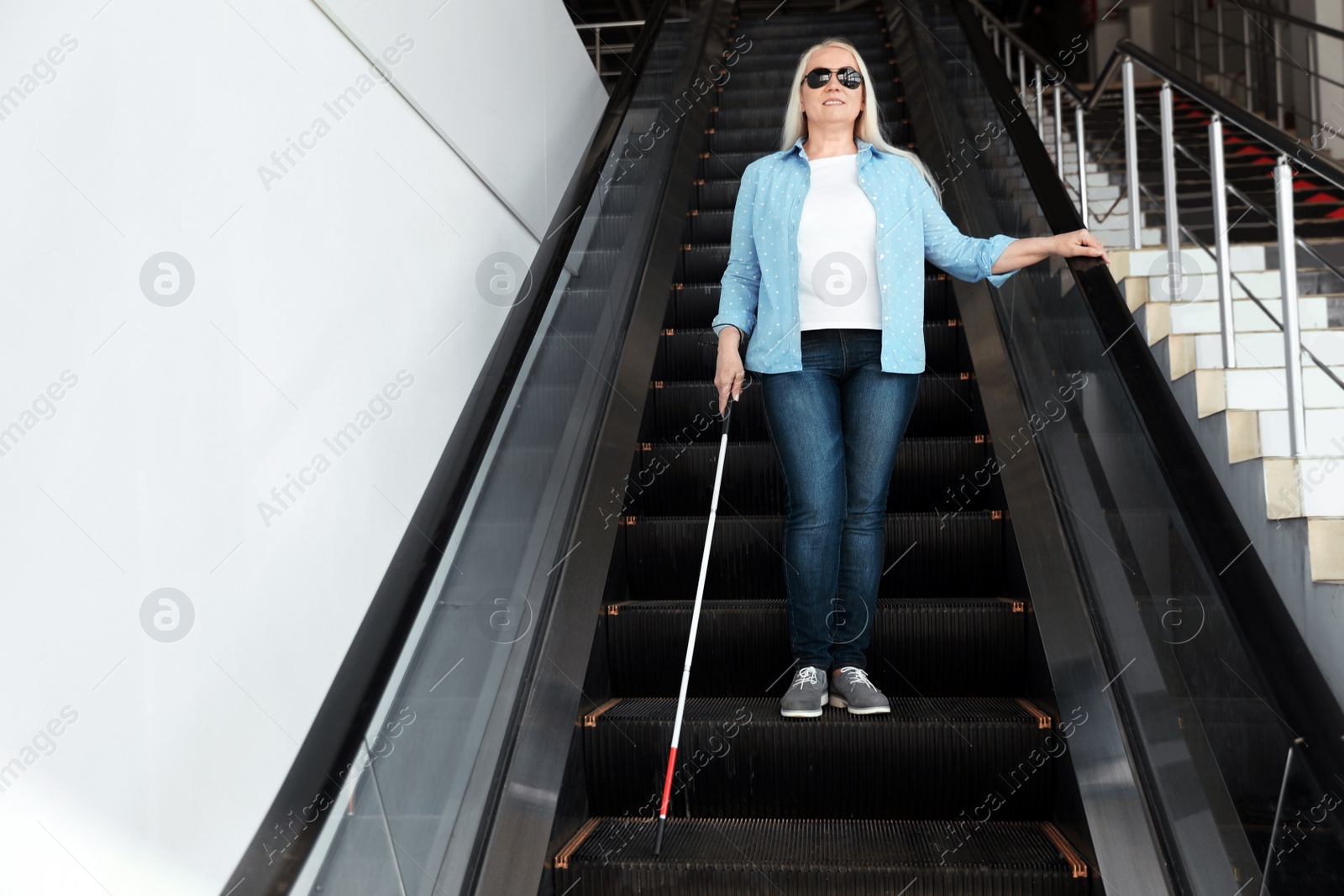 Photo of Blind person with long cane on escalator indoors