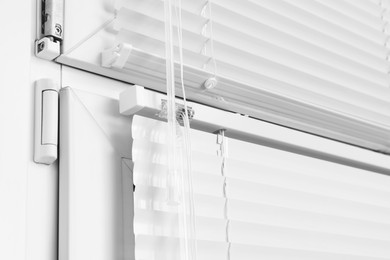 Photo of Window with closed white horizontal blinds and control system indoors, closeup