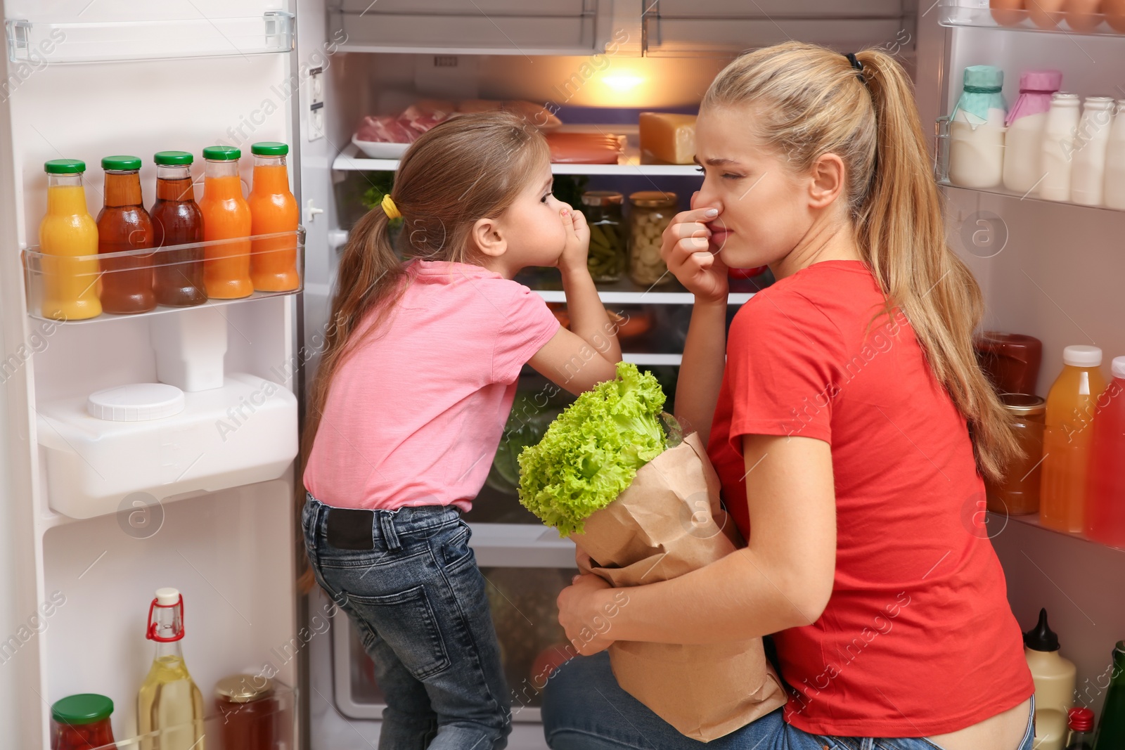 Photo of Young mother and daughter holding noses cause of bad smell from refrigerator at home