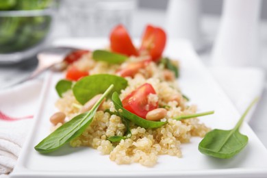 Delicious quinoa salad with tomatoes, beans and spinach leaves served on table, closeup