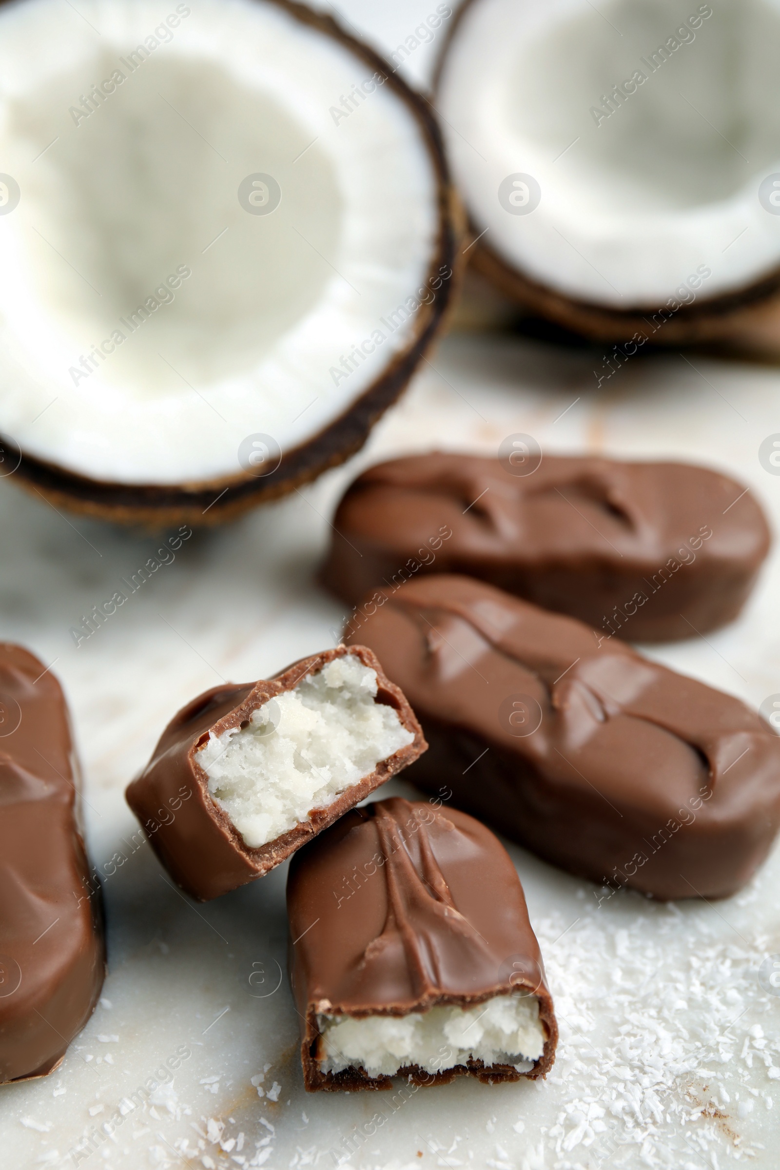 Photo of Delicious milk chocolate candy bars with coconut filling on white table, closeup