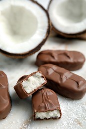 Photo of Delicious milk chocolate candy bars with coconut filling on white table, closeup