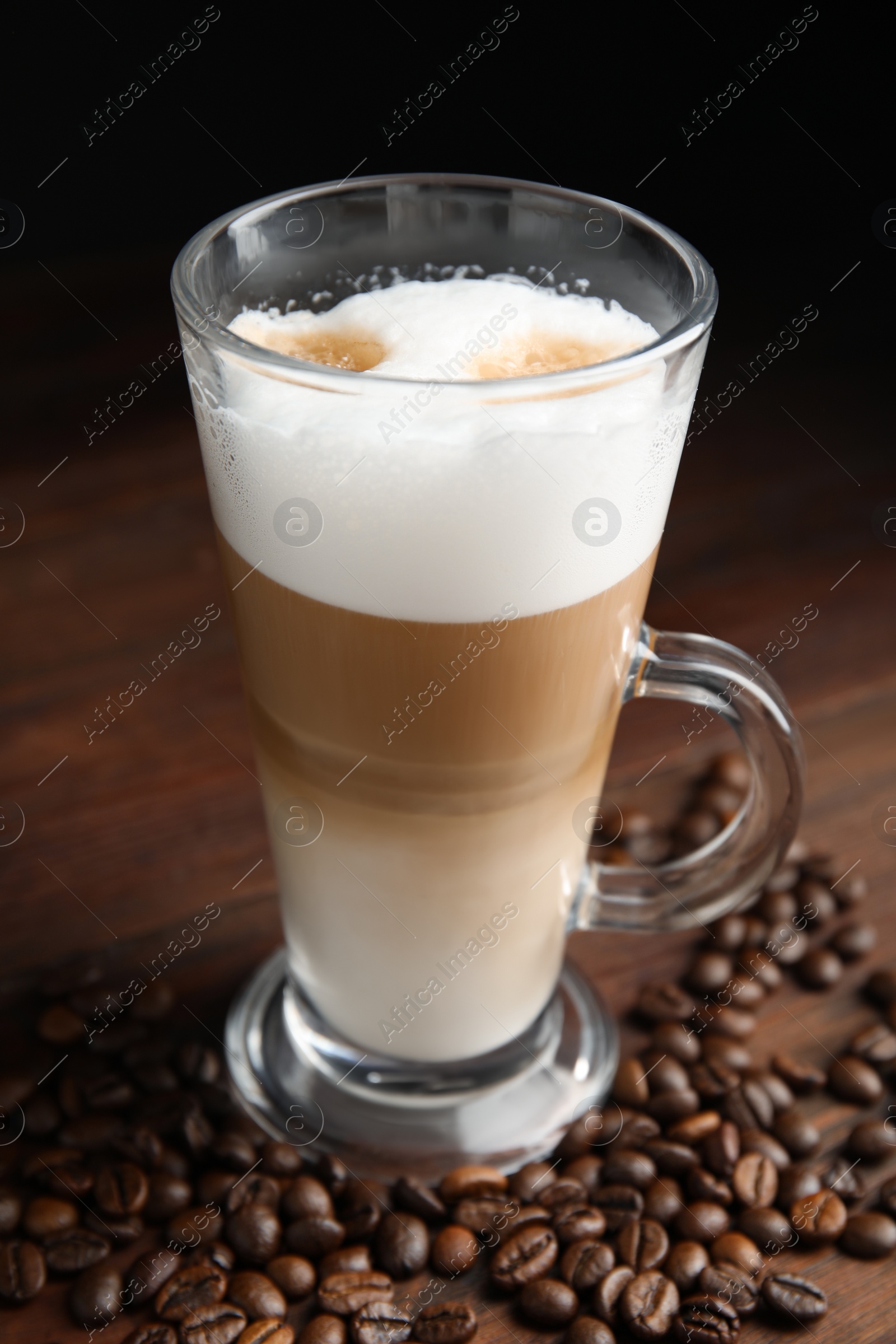 Photo of Delicious latte macchiato and coffee beans on wooden table