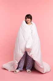 Happy woman in pyjama wrapped in blanket on pink background