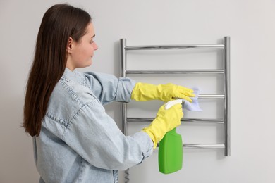 Photo of Woman cleaning heated towel rail with sprayer and rag